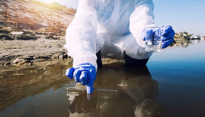 Unrecognizable ecologist taking samples of water with test tube from city river to determine level of contamination and pollution.